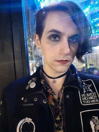 me, wearing my goth battlejacket, a floral shirt, a pentagram choker, red lipstick and eyeshadow